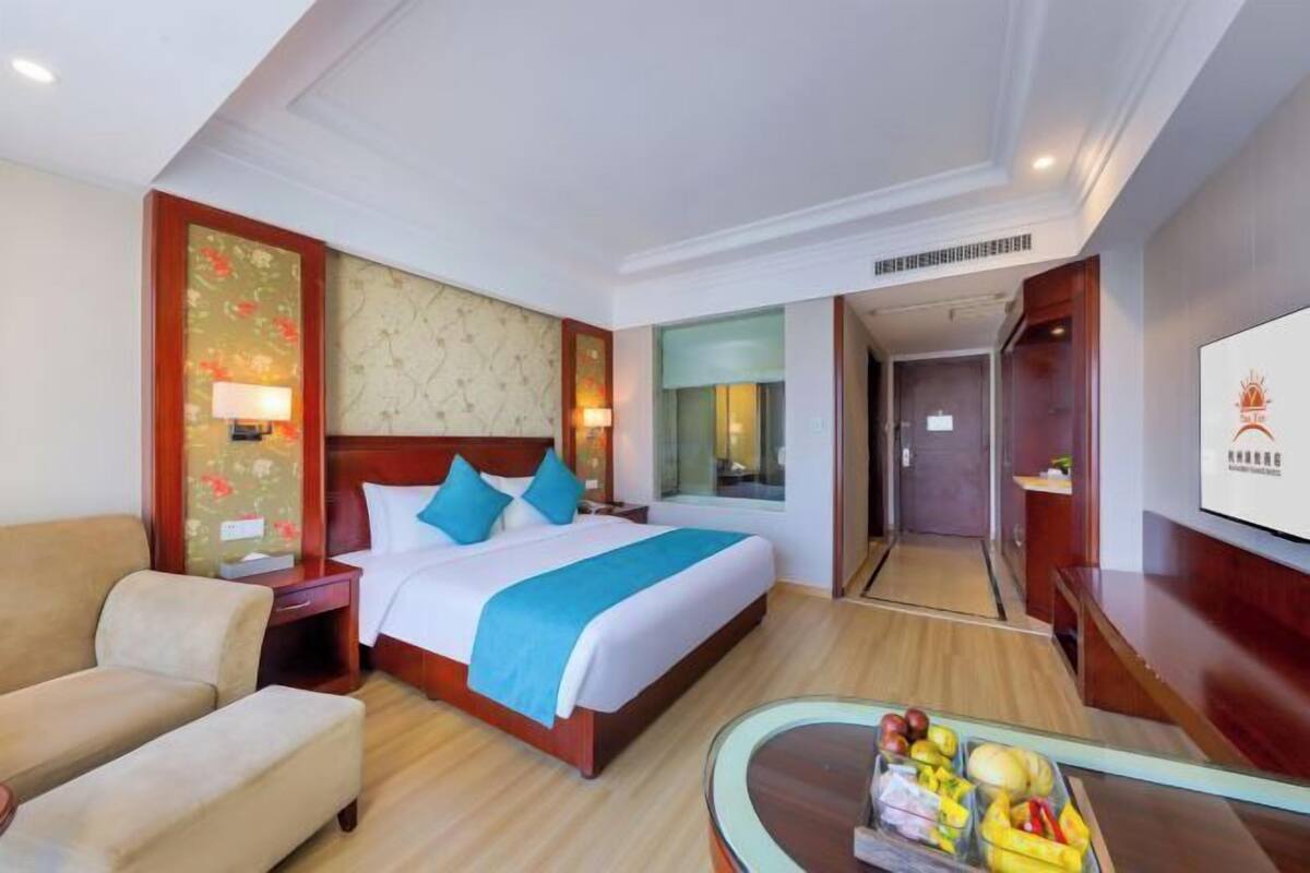 A hotel room with a bed, a desk with fruit, a sofa, and a mirror.