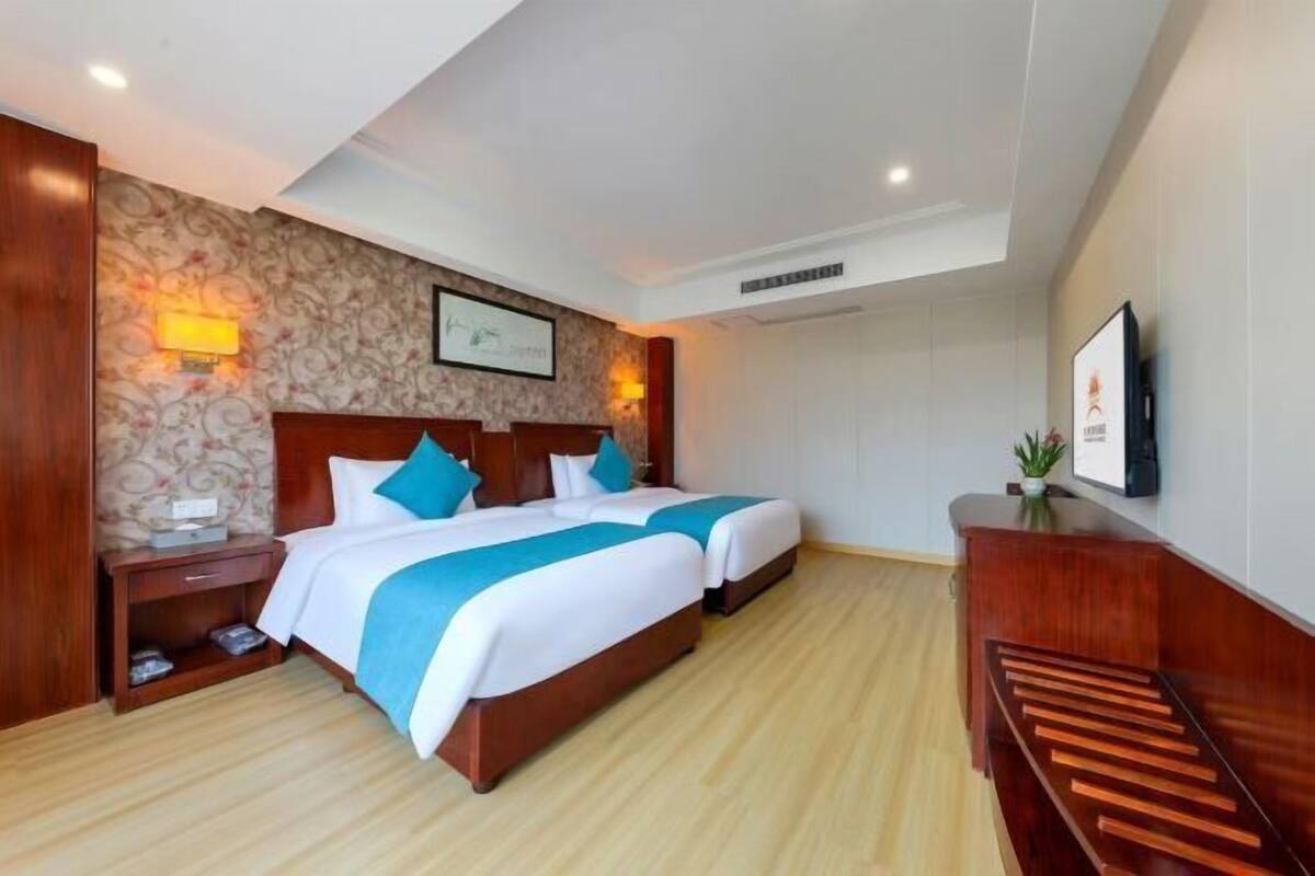 A hotel room with two beds, wooden headboards, a nightstand, a desk, and a wall-mounted TV.