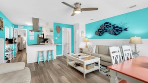 A modern living room with a kitchen, teal walls, white furniture, and a ceiling fan. - 200 Steps to the Beach (Miramar Beach)