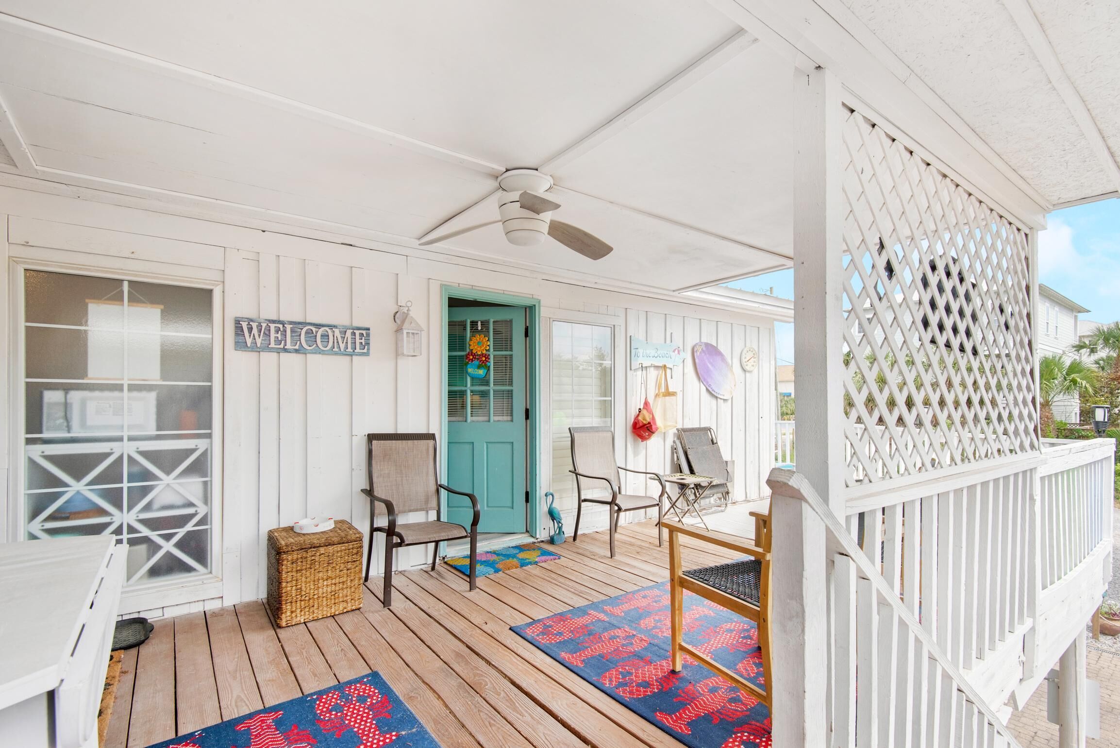 A porch with a 'WELCOME' sign, a teal door, wicker baskets, and outdoor furniture.