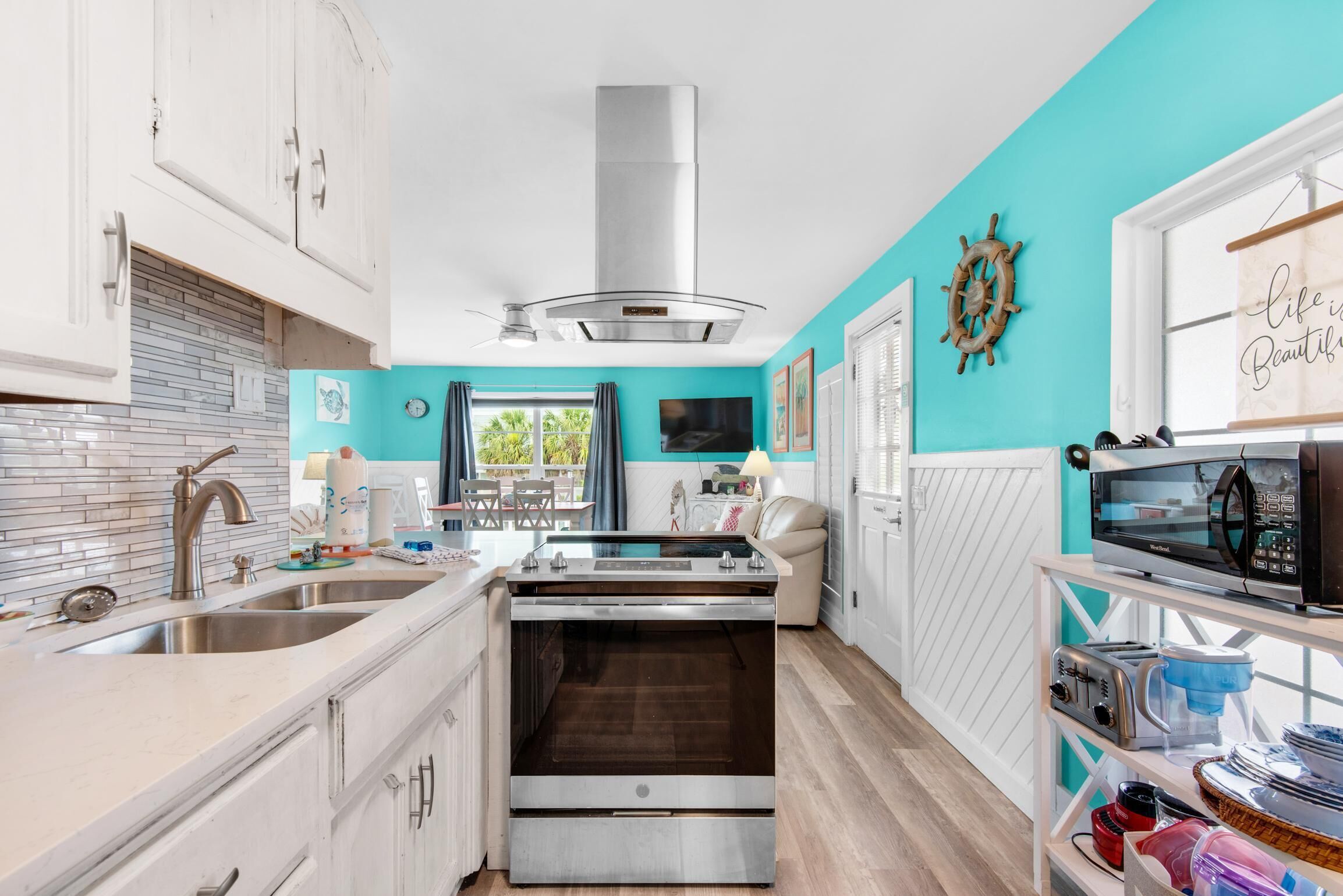 Una cocina moderna con armarios blancos, campana de acero inoxidable, horno empotrado y una ventana con cortinas.