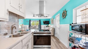 A modern kitchen with white cabinets, a stainless steel range hood, a built-in oven, and a window with curtains. - 200 Steps to the Beach (Miramar Beach)