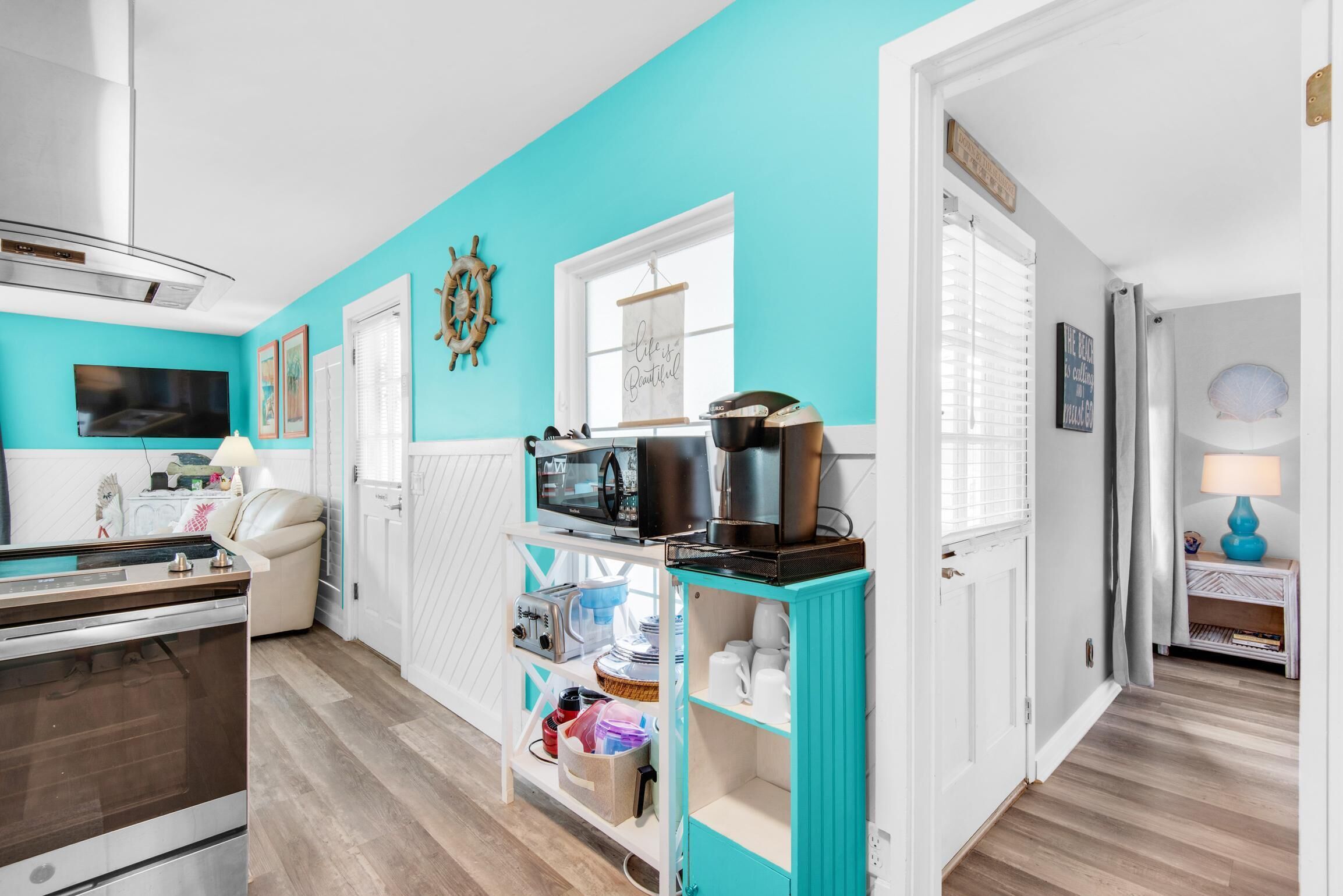 A modern kitchen with a teal accent wall, a built-in oven, and a coffee machine on a teal shelf.