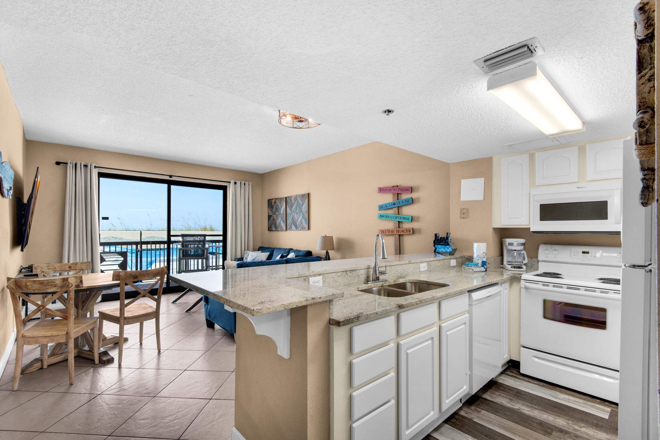 A kitchen with a large island, white cabinets, and a view to the beach.