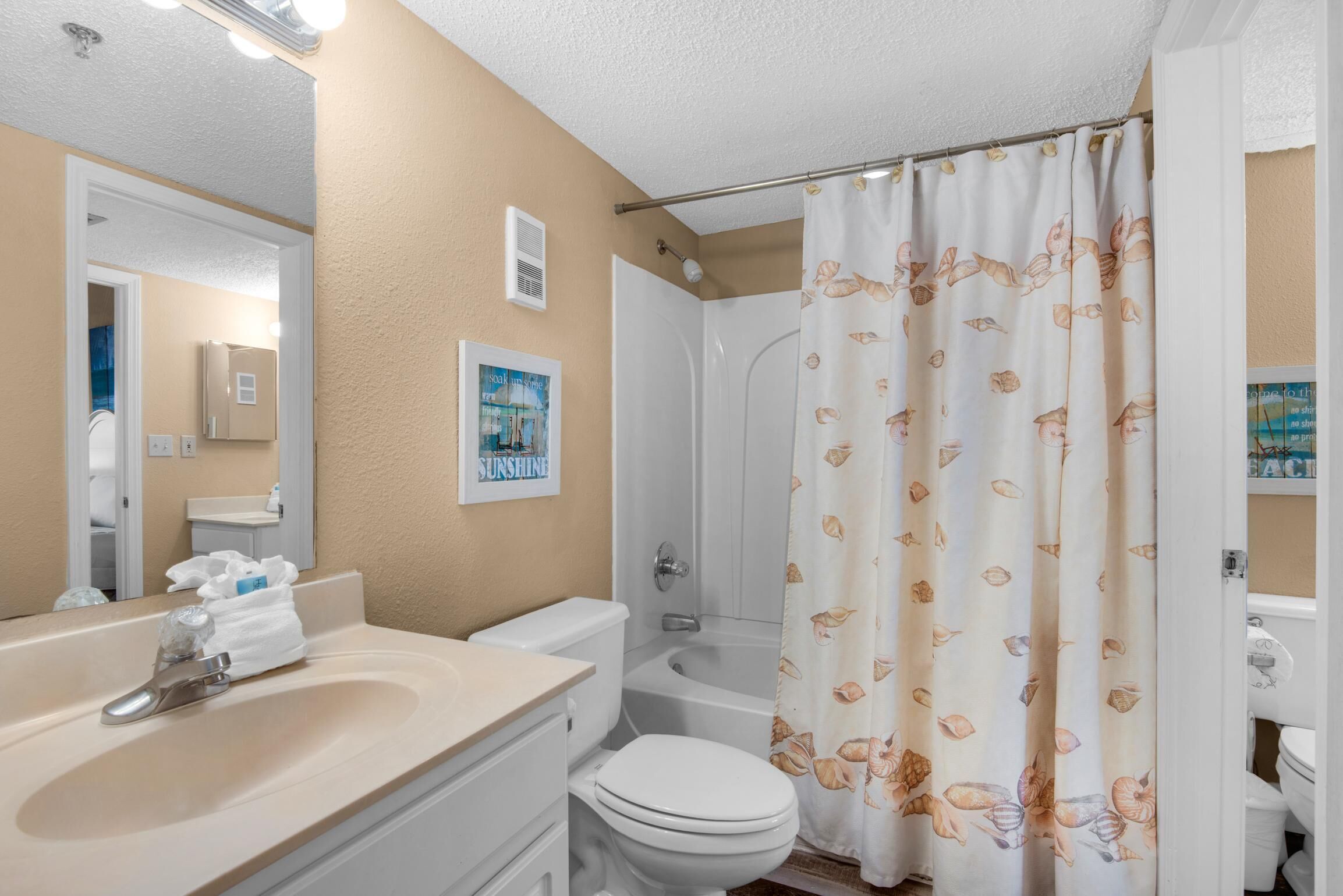 A bathroom with a beige wall, a white sink, a toilet, a shower with a curtain, and a mirror.