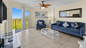 A spacious living room with a balcony, a ceiling fan, a sofa set, a coffee table, and a flat-screen TV. - Family-Friendly 2BR w/ Views, Pool, & Beach (Tavernier)