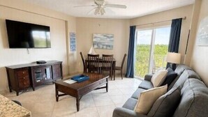 A living room with a sofa, a coffee table, a TV, and a dining area with chairs and a table. - Couples' Retreat 2BR w/ Ocean Views, Pool & Beach (Tavernier)