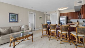 A modern kitchen with a refrigerator, stove, and dining area with wicker chairs. - Key Largo 2BR - Partial Ocean Views, Pool & Beach (Tavernier)