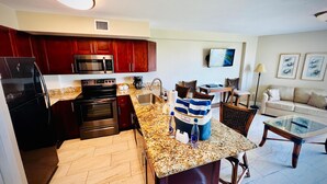 A modern kitchen with dark red cabinets, stainless steel appliances, and a granite countertop. - Key Largo 2BR - Partial Ocean Views, Pool & Beach (Tavernier)