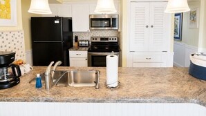A kitchen with a stainless steel sink, a black refrigerator, a microwave, a stove, and hanging pendant lights. - 2BR Condo w/ Ocean Views, Tropical Landscaping, Pool (Tavernier)