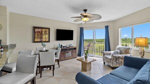 A spacious living area with a ceiling fan, a flat-screen TV, a dining table with chairs, a sofa, and a balcony with a view. - 2BR Condo w/ Ocean Views, Private Beach & Pool (Tavernier)