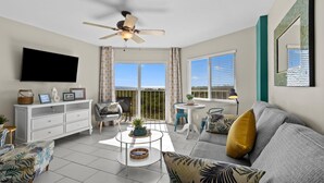 A modern living room with a ceiling fan, a flat-screen TV, a sofa, a coffee table, and a balcony with curtains.