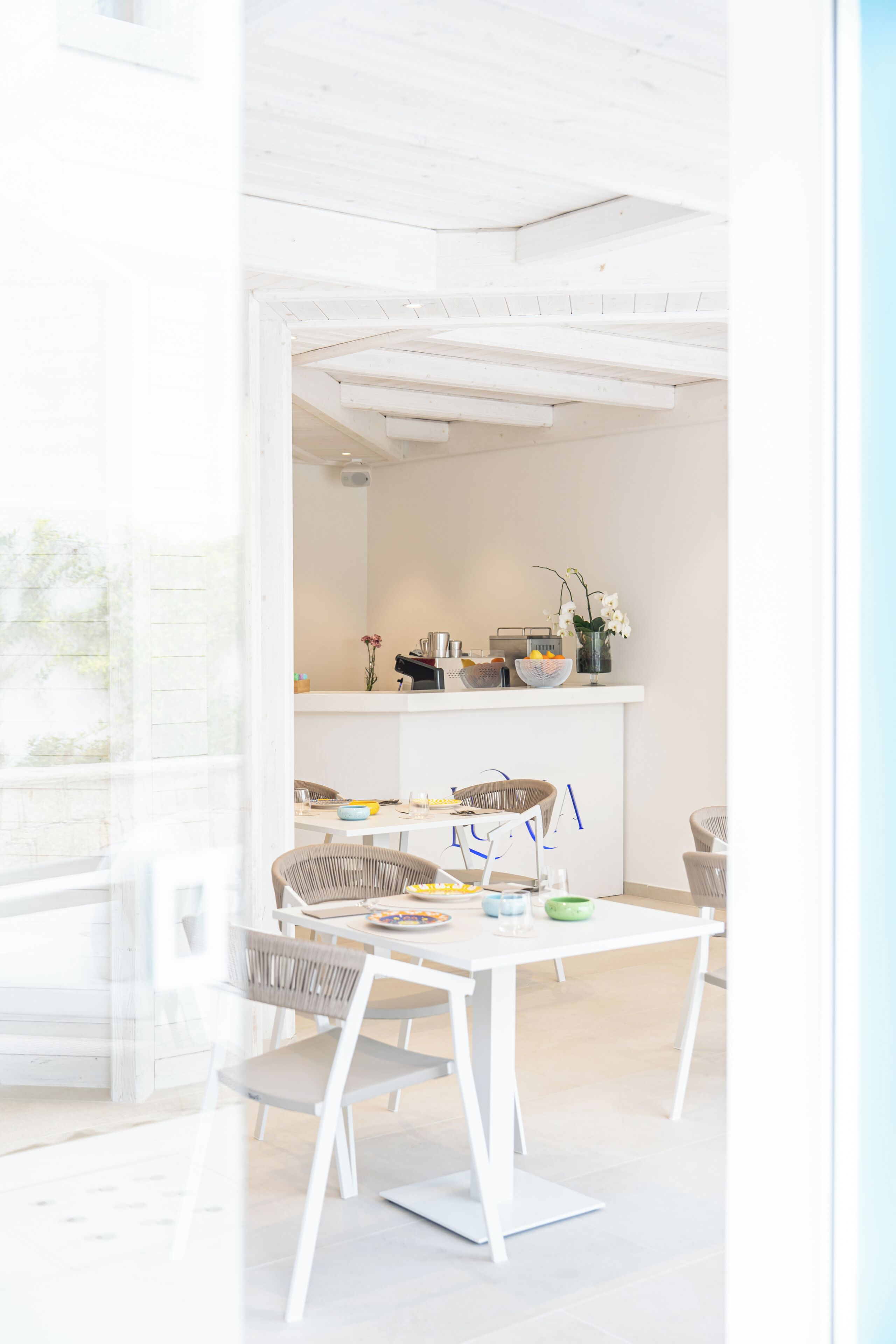 Une cuisine lumineuse et moderne, avec des meubles blancs, un coin repas comprenant une table et des chaises blanches, et une vue sur l’extérieur grâce à une porte vitrée.
