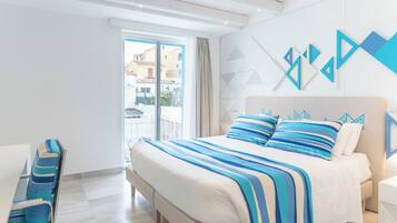 A modern hotel room with a large bed, a seating area with blue-striped chairs, and a view of buildings through the window.