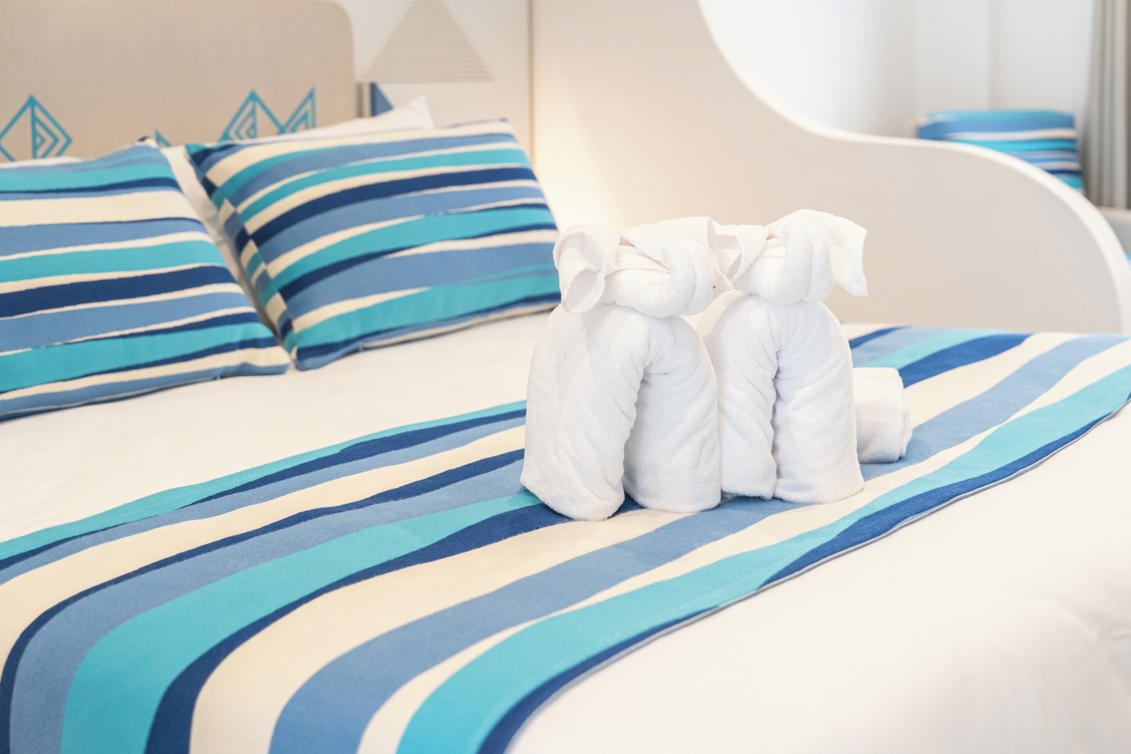 Une chambre d’hôtel avec un lit doté de draps à rayures, d’une tête de lit blanche et de serviettes soigneusement pliées.