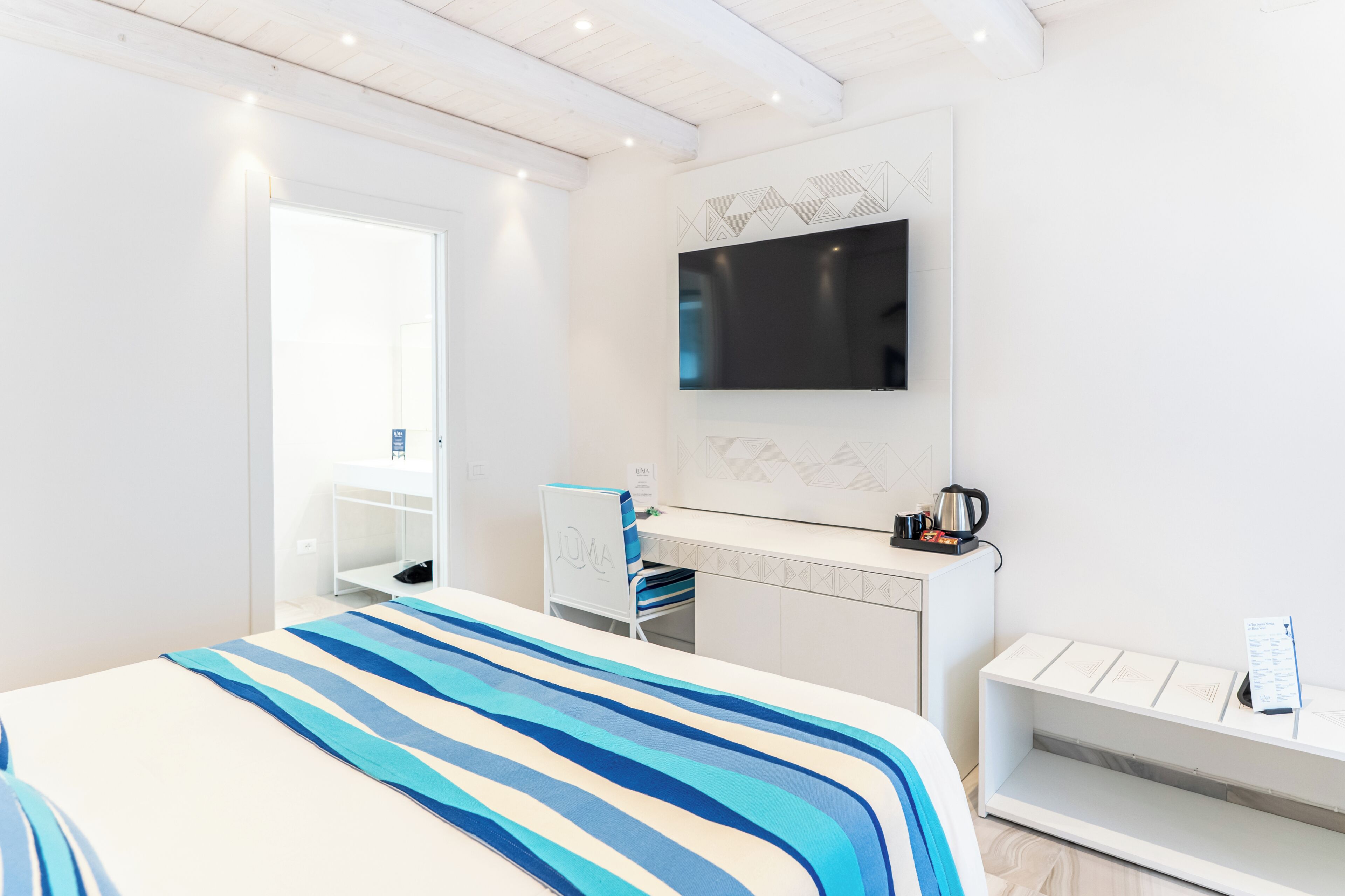 Een moderne hotelkamer met een bed, bureau, stoel, televisie en minibar.