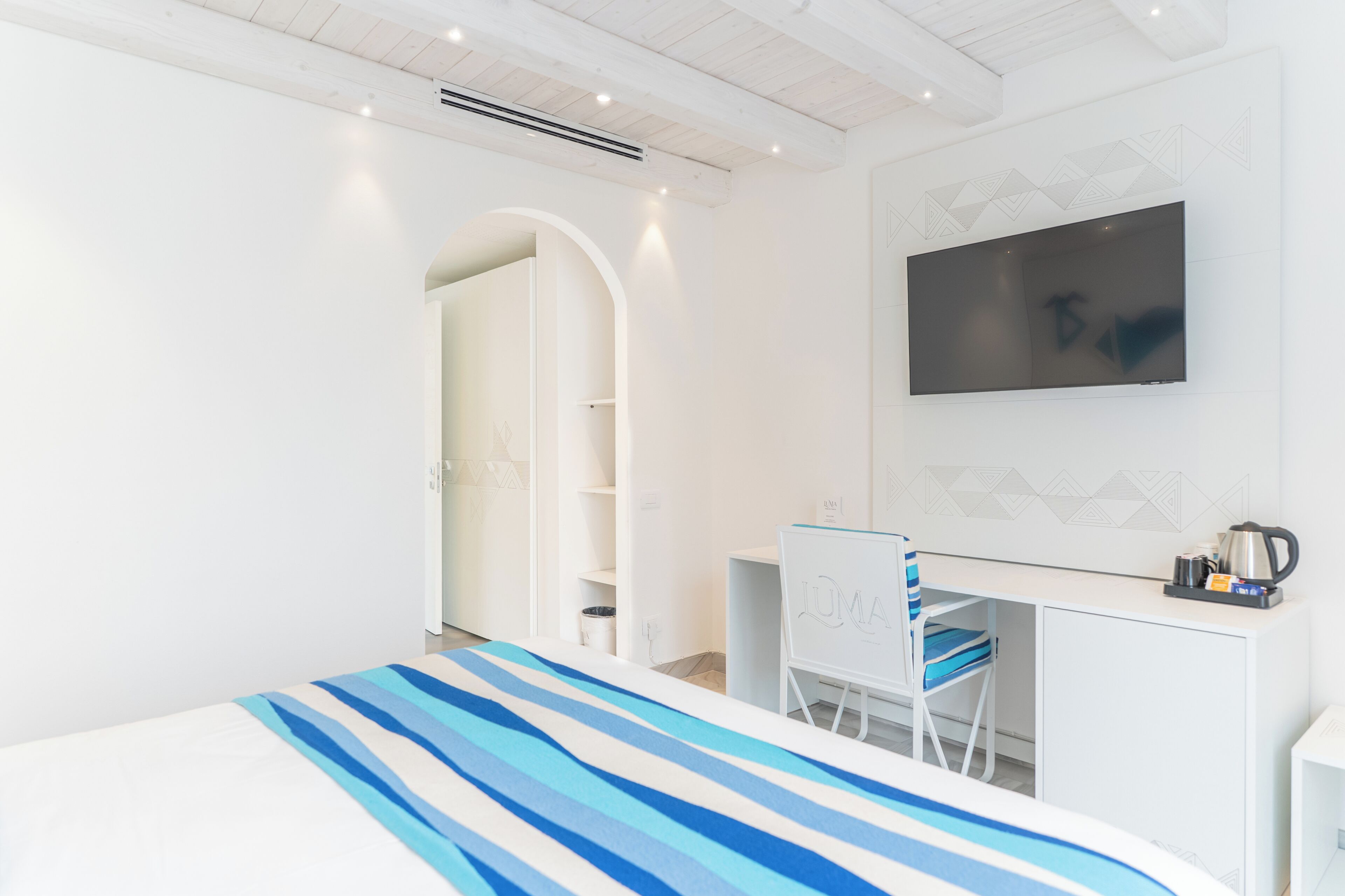 Une chambre d’hôtel moderne équipée d’un lit, d’un bureau, d’une chaise, d’une télévision et d’une armoire.