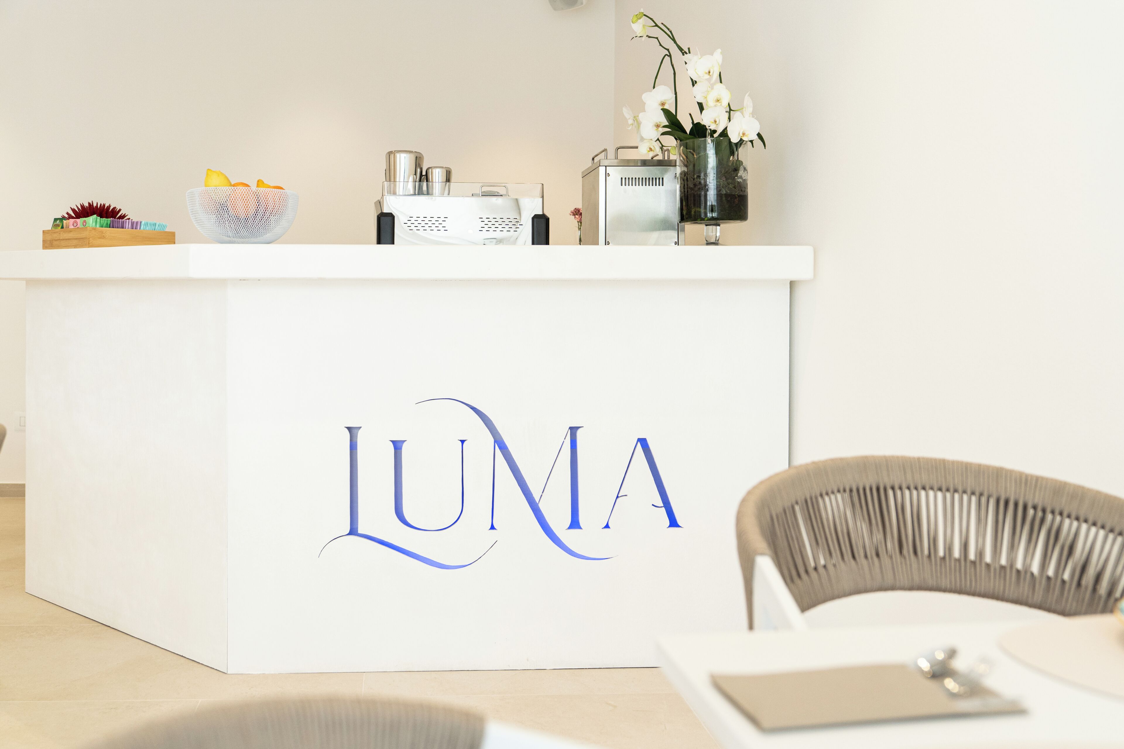 Balcão de recepção com o logo 'LUMA', uma cadeira branca e um vaso com flores.