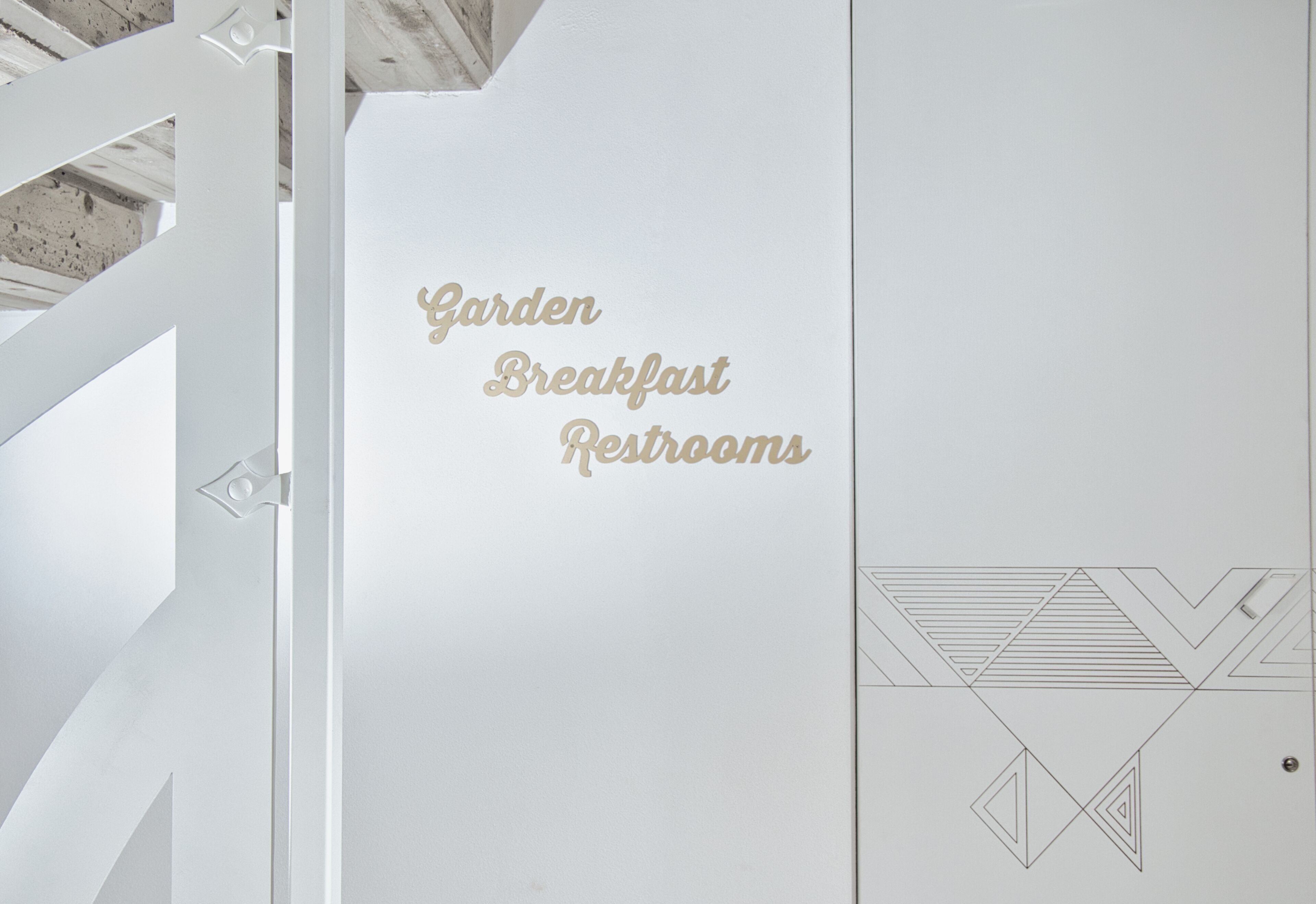 Schild mit der Aufschrift 'Gartenfrühstück Toiletten' in einem modernen, weißen Innenraum.