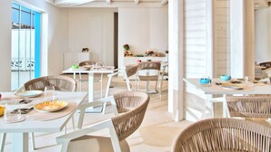 Un comedor luminoso con mobiliario blanco, vistas al exterior y un techo con vigas a la vista.