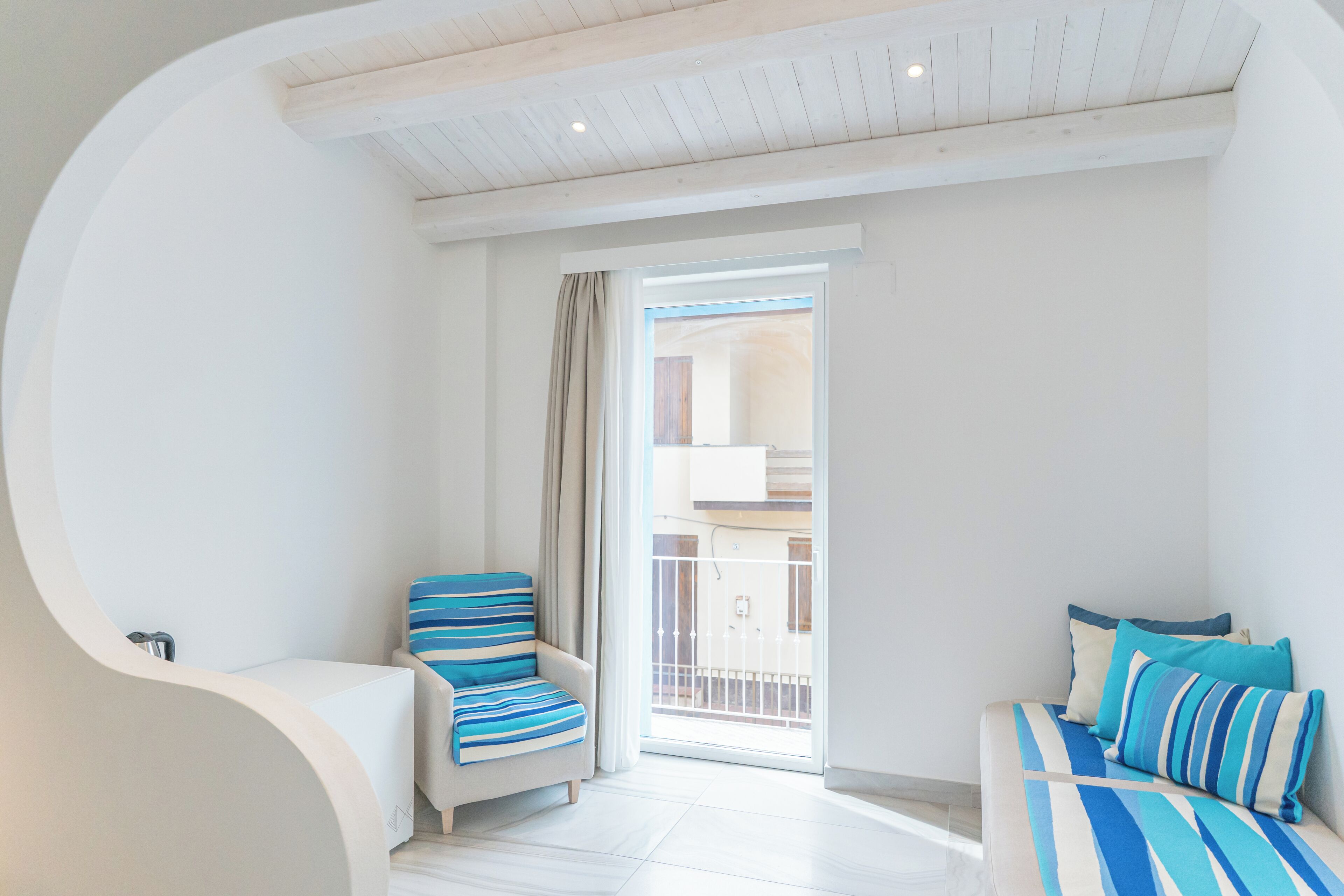 A bedroom with a bed, a chair, and a balcony.