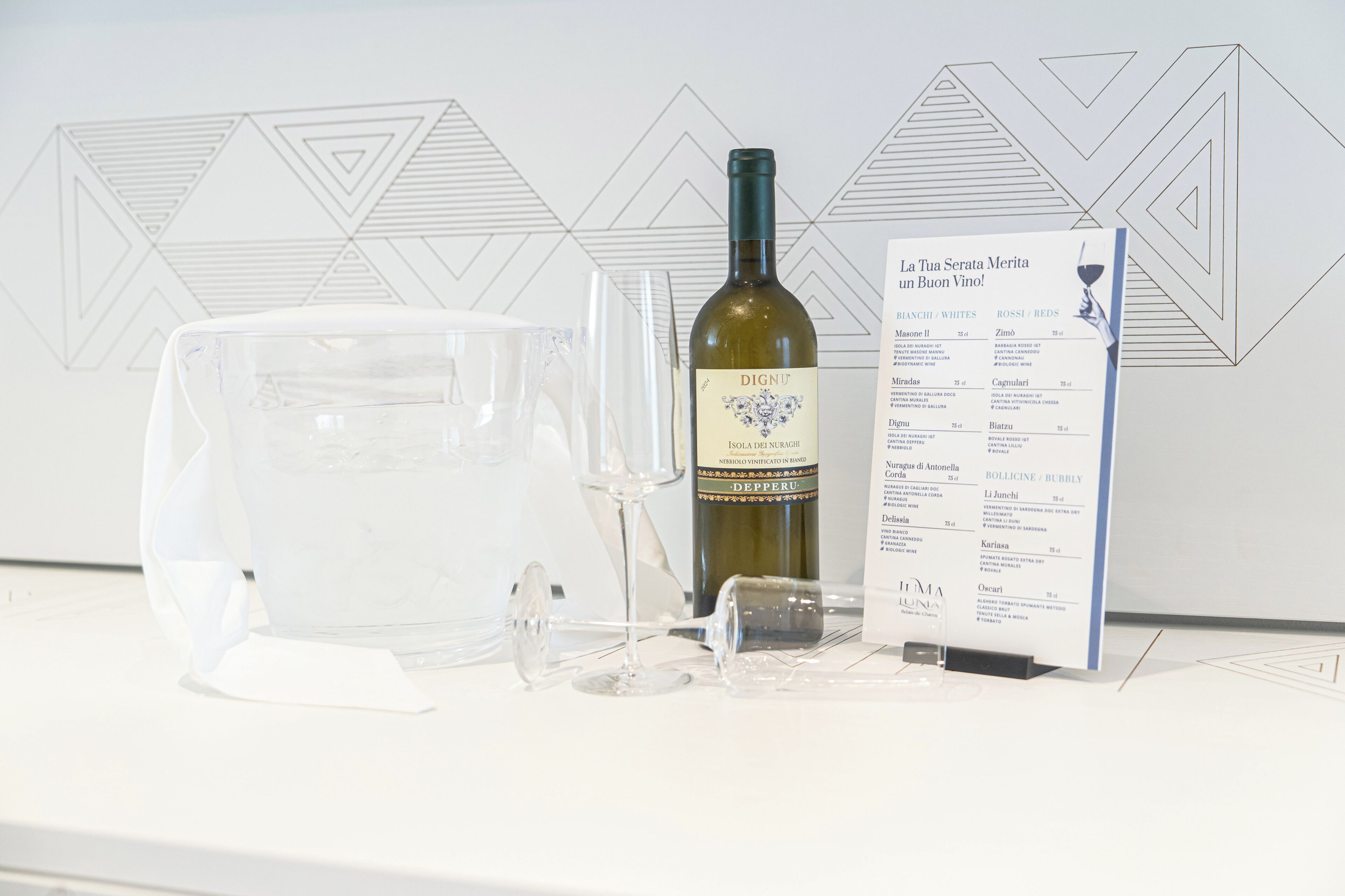 A wine bottle, glasses, and a menu on a table with a geometric wall pattern.