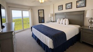 A bedroom with a large bed, a dresser, a nightstand, and a ceiling fan. There is a sliding glass door leading to a balcony. - 2BR Condo w/ Ocean View, Pool & Tropical Setting (Tavernier)