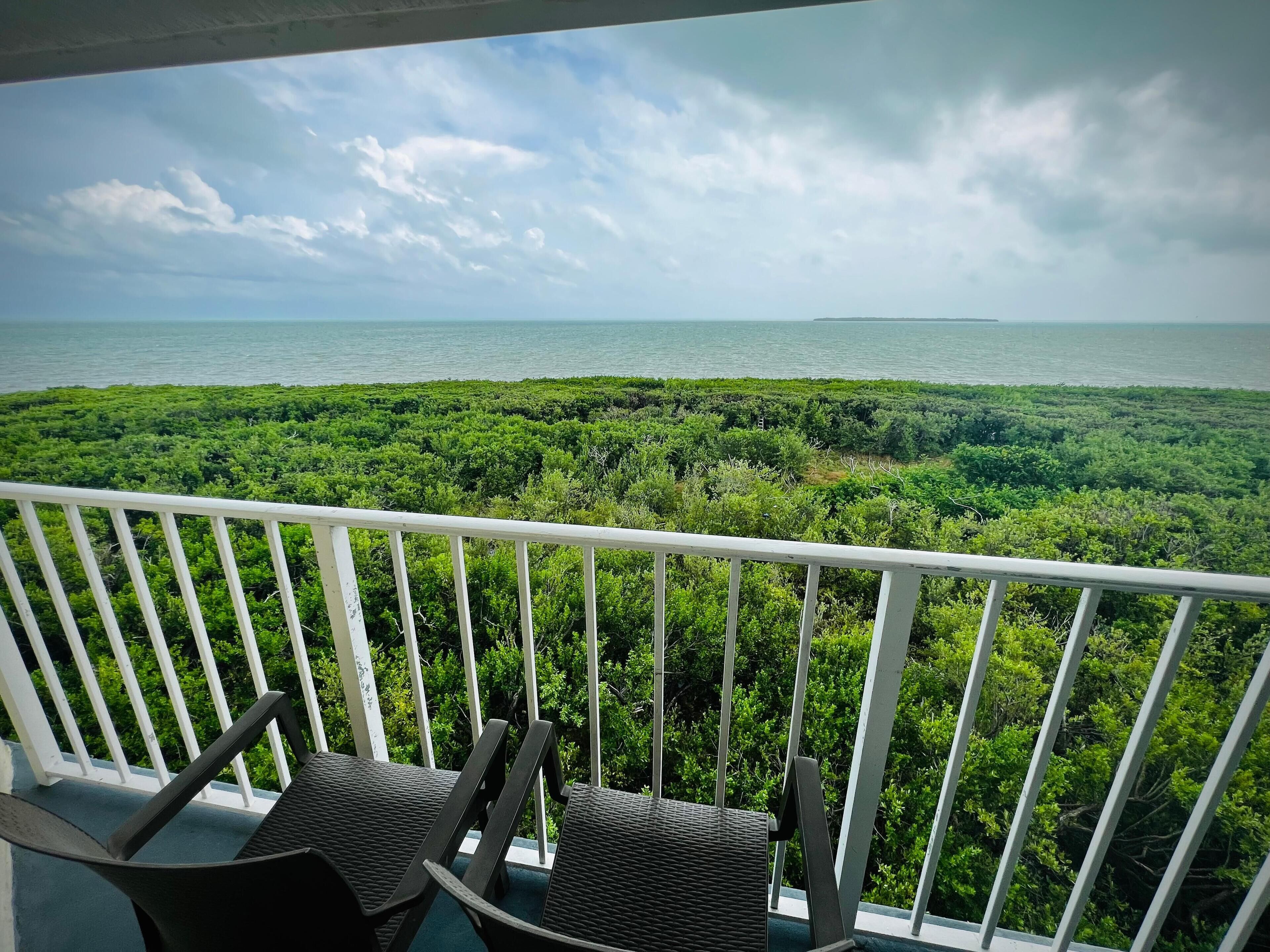 Un balcon avec deux chaises donnant sur un paysage verdoyant et luxuriant, ainsi que sur une étendue d’eau.