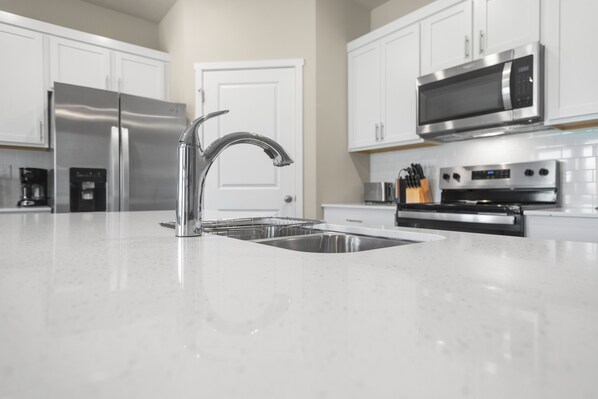 A modern kitchen with stainless steel appliances, a white countertop, and a double sink.