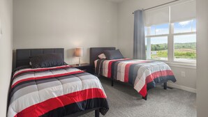 A bedroom with two beds, a window with curtains, and a view of greenery outside.