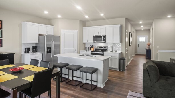 A modern kitchen with white cabinets, a central island, and a dining area with a black table and chairs.