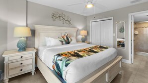Une chambre à coucher avec un lit, deux tables de chevet avec des lampes, un ventilateur de plafond, une porte blanche et un placard.