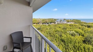 A balcony with a chair, overlooking a lush green landscape and a building in the distance.