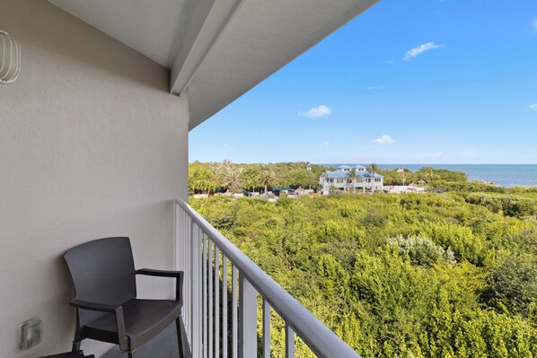 A balcony with a chair, overlooking a lush green landscape and a building in the distance. - Hideaway in Key Largo 2BR Condo - Ocean View, Pool (Tavernier)