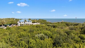 A coastal property with a large house, dense greenery, and a clear view of the ocean.