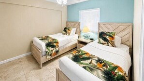 A bedroom with two beds, a ceiling fan, a nightstand with a lamp, and a window with blinds.