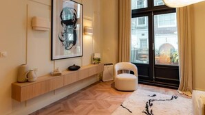 Una sala de estar moderna con piso de madera, un sillón blanco, un ventanal con cortinas, una obra de arte colgada en la pared y una estantería empotrada con objetos decorativos.