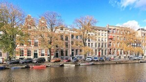 Un canal con barcos, una hilera de edificios tradicionales y árboles otoñales.