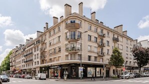 Un edifici de diverses plantes amb balcons, botigues i cotxes aparcats.