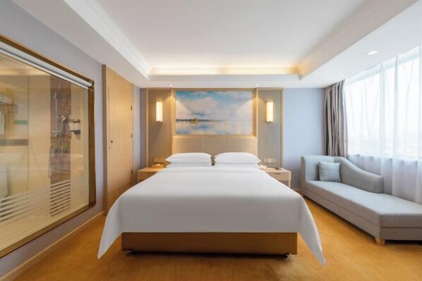 A hotel room with a large bed, a sofa, a painting on the wall, and a view of the outdoors. - Vienna Hotel (Renhe subway station store of Guangzhou Baiyun International Airport) (Guangzhou)