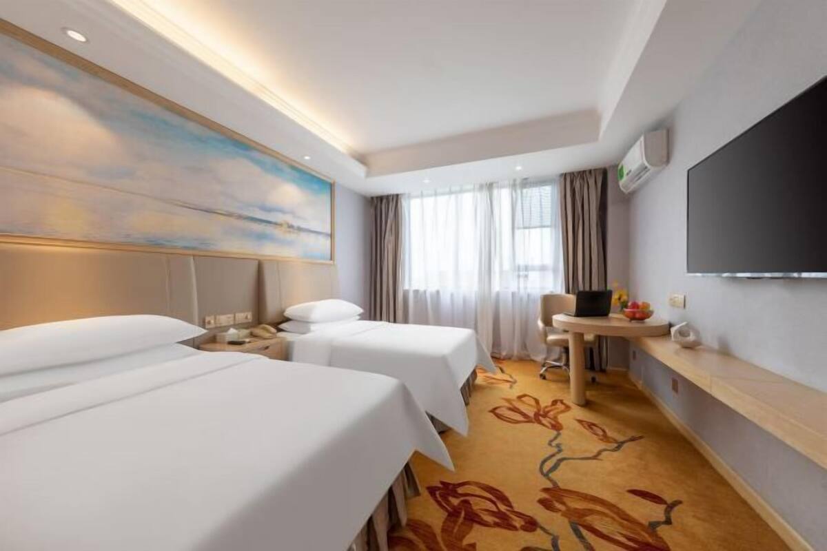 Ein Hotelzimmer mit zwei Betten, einem Schreibtisch, einem Stuhl, einem Fernseher und einem großen Fenster mit Vorhängen.