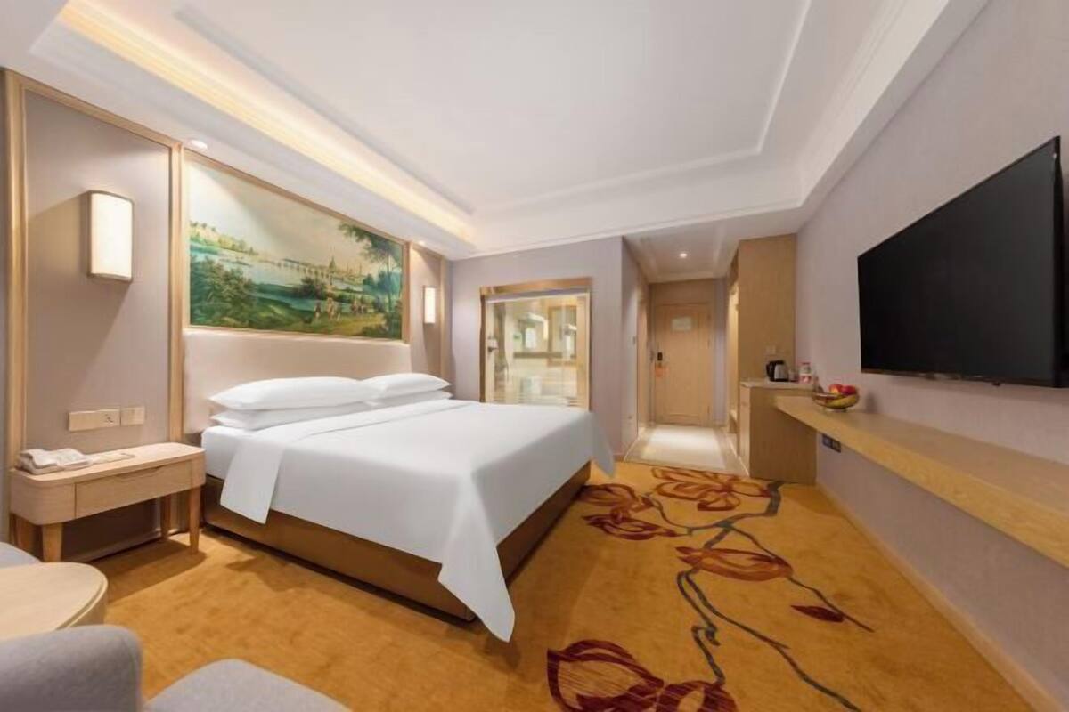 Ein modernes Hotelzimmer mit einem großen Bett, einem Flachbildfernseher, einem Bild an der Wand und einem floralen Teppich.