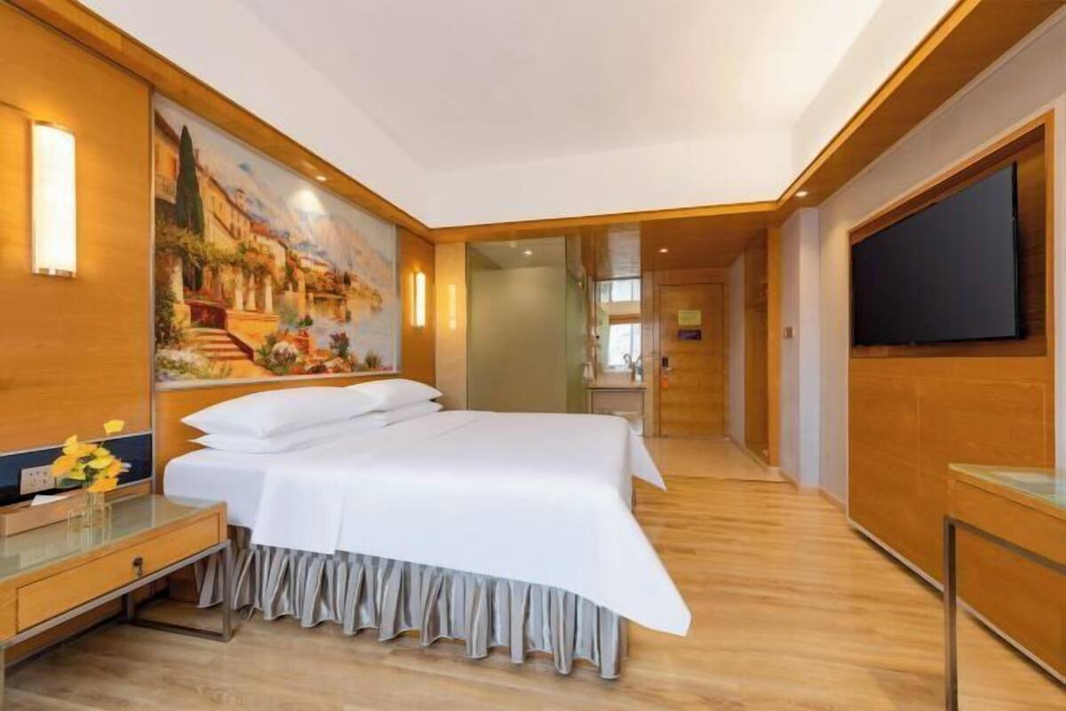 Ein Hotelzimmer mit einem großen Bett, einem Gemälde an der Wand, einem Fernseher und einem Holzboden.