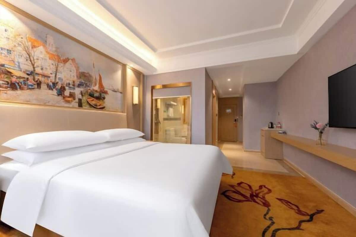 Una habitación de hotel con cama, un cuadro en la pared, televisión y escritorio.