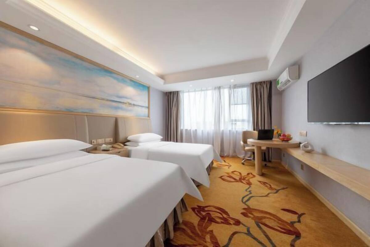 Ein Hotelzimmer mit zwei Betten, einem Schreibtisch, einem Sessel, einem Flachbildfernseher und einem großen Wandbild.