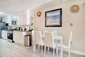 Une cuisine moderne avec des meubles blancs, une cuisinière en acier inoxydable et un coin repas comprenant des chaises blanches et une table en verre.