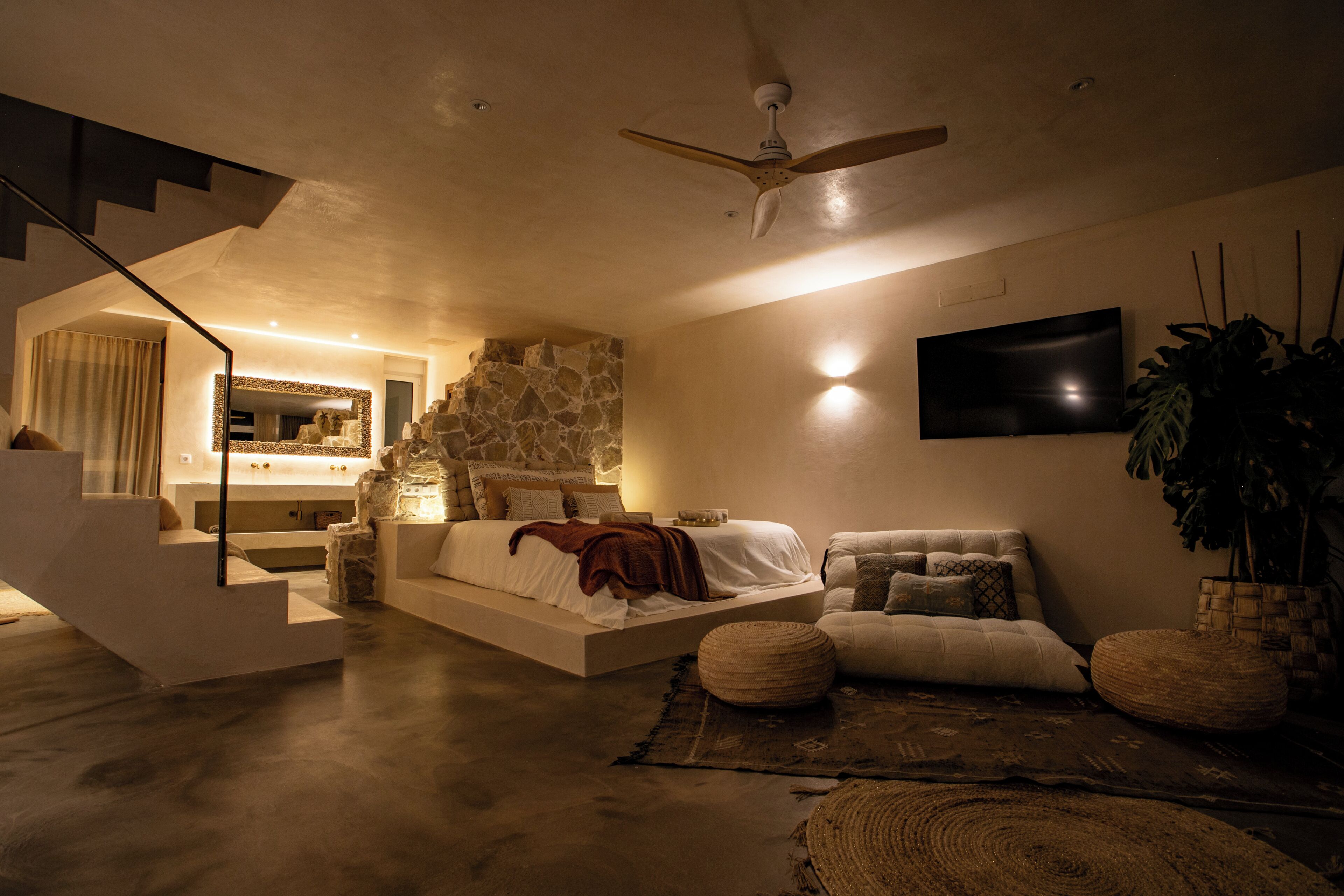 Une chambre moderne avec un mur d’accent en pierre, un grand lit, un téléviseur à écran plat et un escalier.