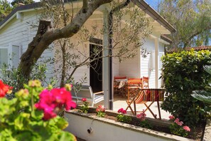 Una casa con porche, mobiliario exterior y un jardín lleno de flores.