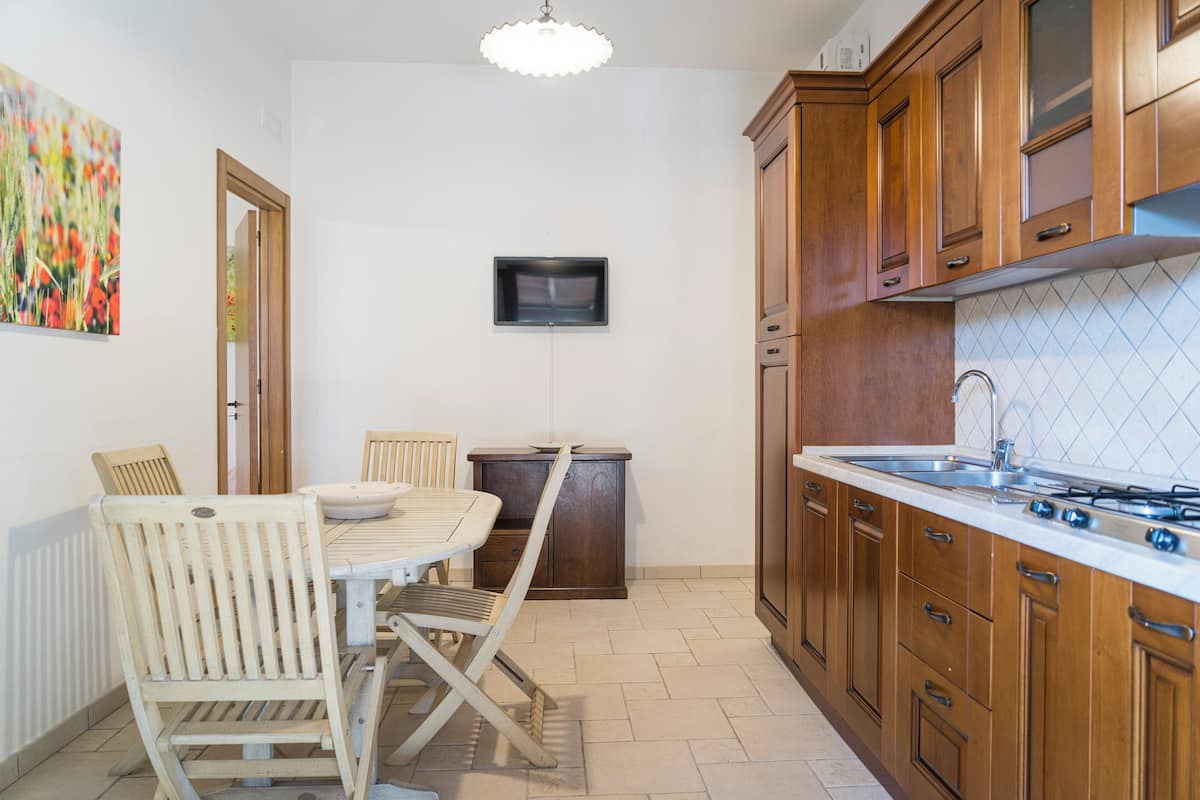 Una cocina compacta con armarios de madera, estufa integrada y un pequeño comedor con mesa y sillas.