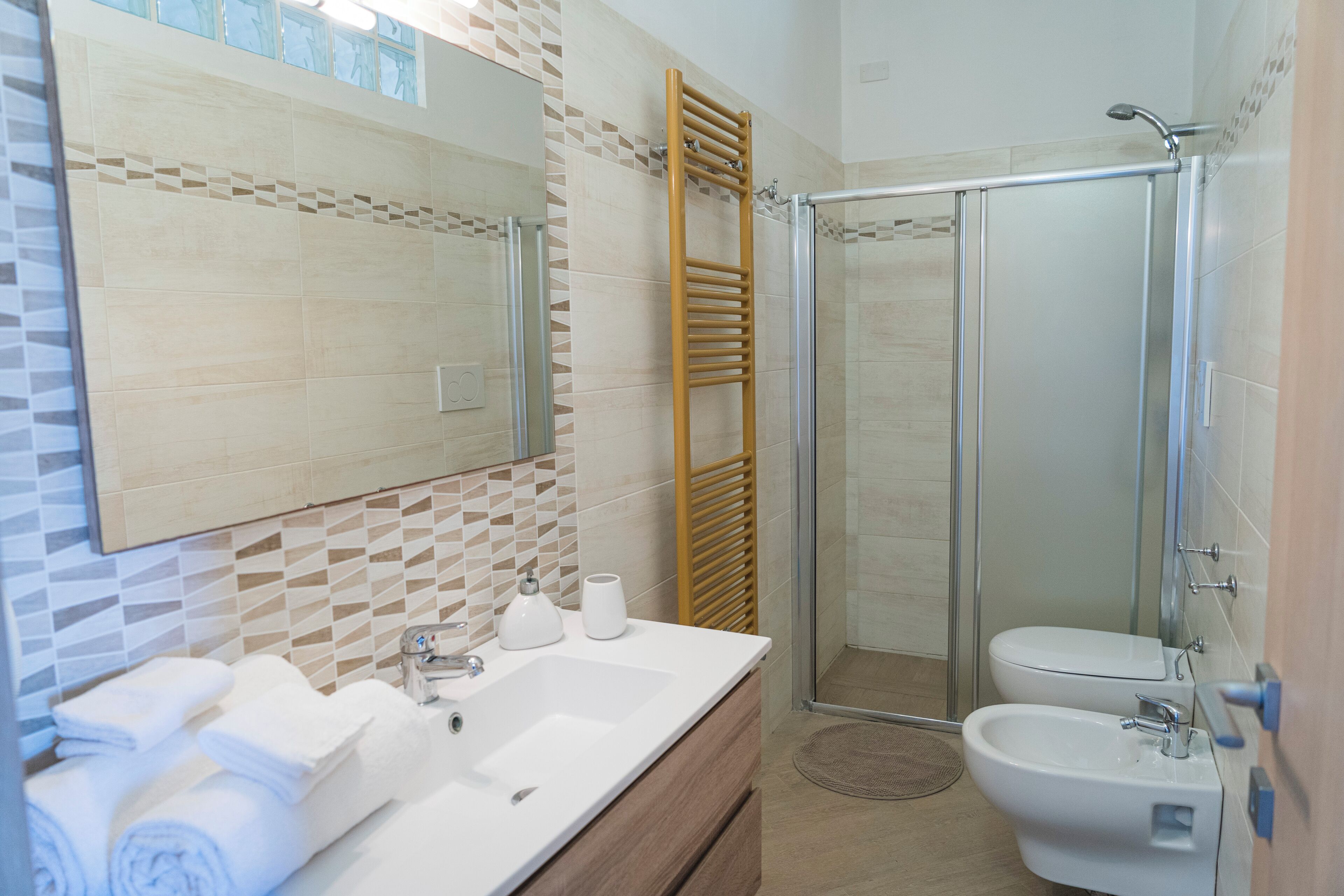 A bathroom with a large mirror, a sink, a bidet, and a glass shower enclosure.